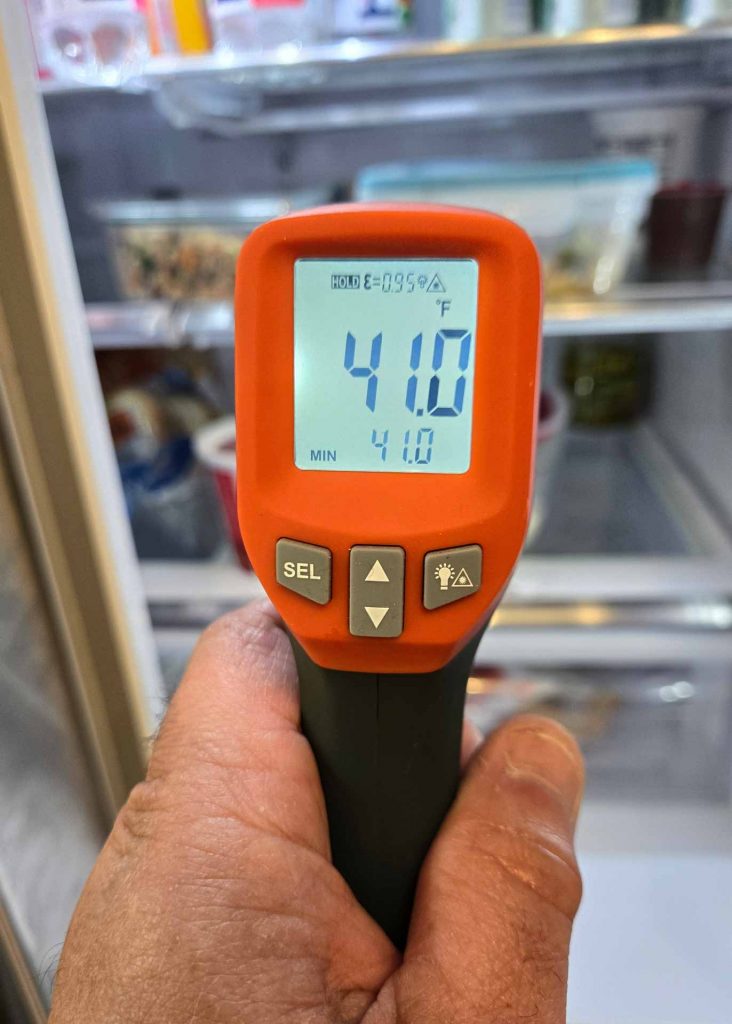 Appliance repair technician holding a thermometer up to a refrigerator, measuring the internal temperature