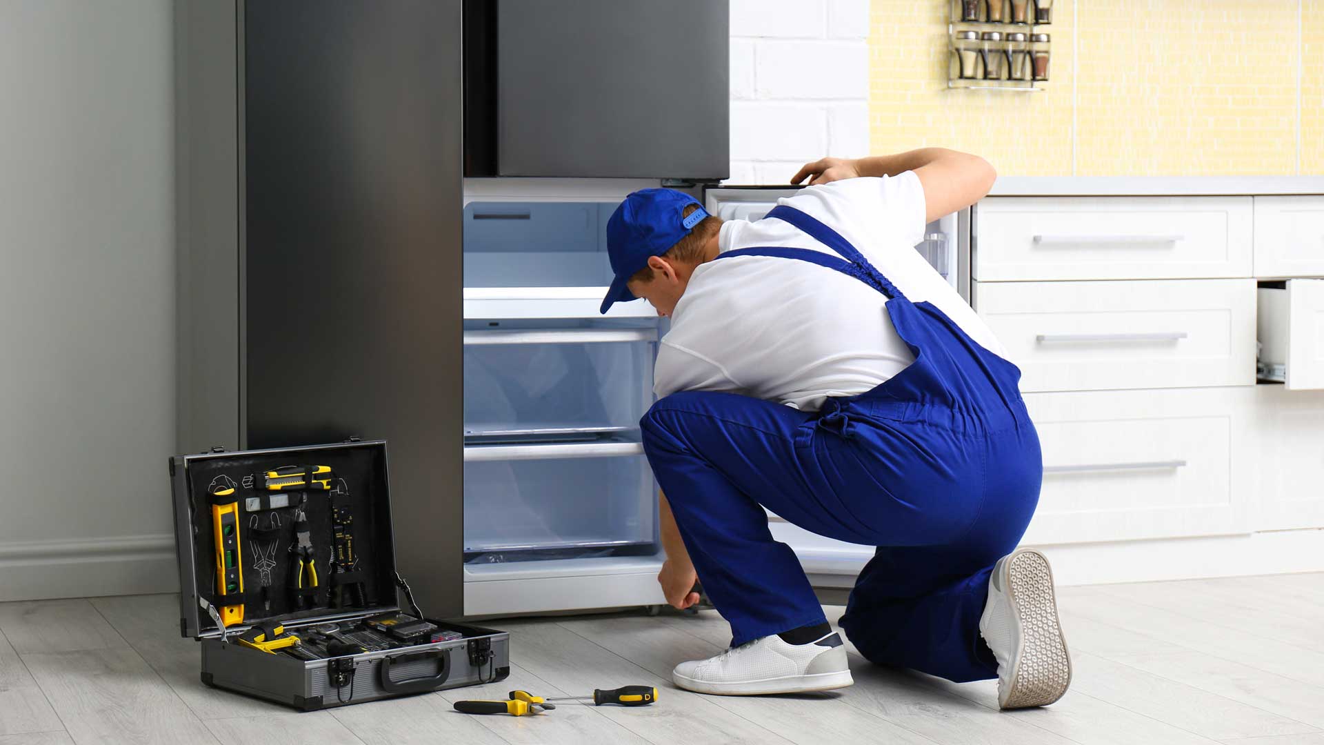 A man in blue overalls repairing the freezer drawer of a refrigerator